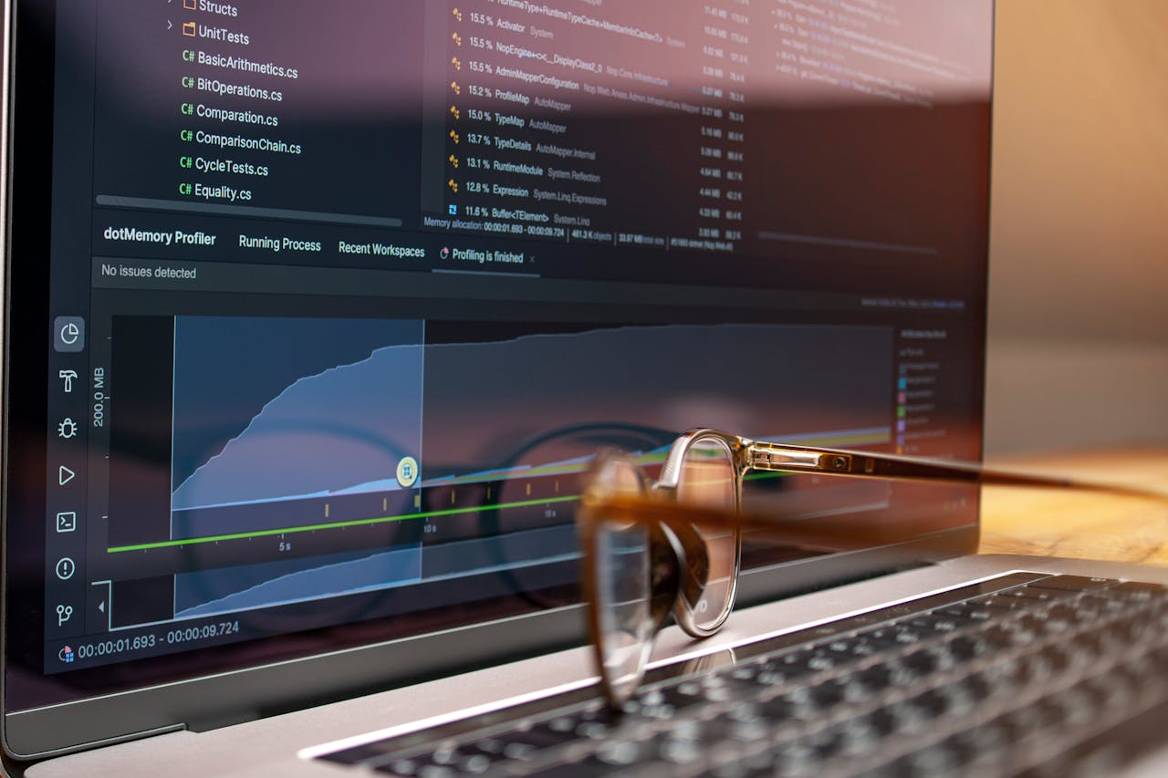 Home Laptop screen displaying code and performance graphs with eyeglasses resting on the keyboard.